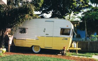 white and yellow travel trailer parked beside fence