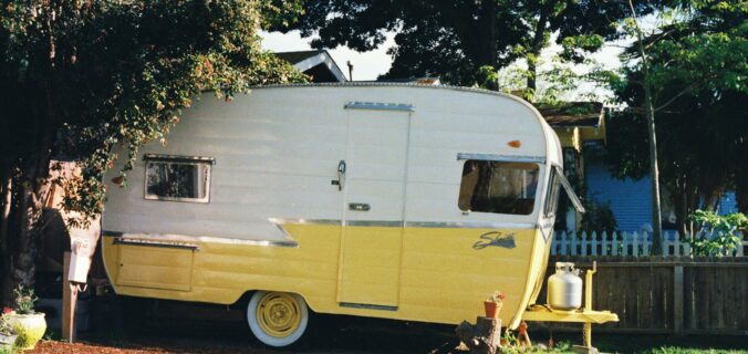 white and yellow travel trailer parked beside fence