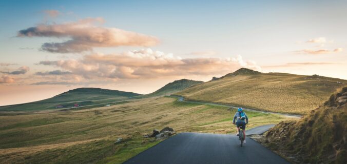 person cycling on road distance with mountain during daytime